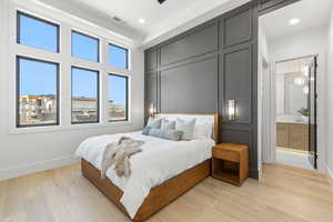 Bedroom featuring light wood-style floors, a decorative wall, ensuite bathroom, and recessed lighting