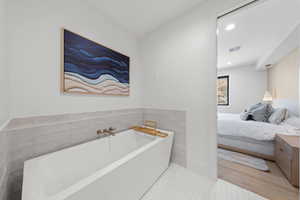 Bathroom with a garden tub, wood finished floors, recessed lighting, tile walls, and ensuite bath