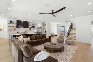 Living room featuring light wood-type flooring, recessed lighting, a ceiling fan, and stairs