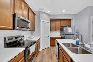 Kitchen with appliances with stainless steel finishes, brown cabinetry, light wood-type flooring, and recessed lighting