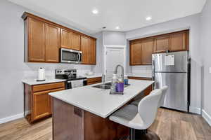 Kitchen featuring a kitchen bar, appliances with stainless steel finishes, brown cabinetry, a kitchen island with sink, and recessed lighting