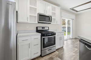 Kitchen featuring appliances with stainless steel finishes, white cabinets, open shelves, light countertops, and light wood-style floors