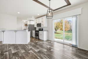 Kitchen featuring a breakfast bar area, stainless steel appliances, white cabinets, dark wood-type flooring, and hanging light fixtures