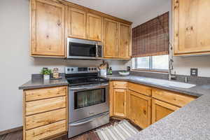 Kitchen with stainless steel appliances, dark wood finished floors, and dark stone countertops