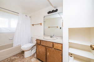 Bathroom featuring vanity, shower / bathtub combination with curtain, and light stone finish floors