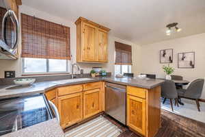 Kitchen featuring appliances with stainless steel finishes, a peninsula, dark wood finished floors, a textured ceiling, and dark countertops