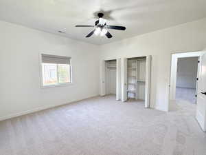 Unfurnished bedroom with two closets, light carpet, and ceiling fan