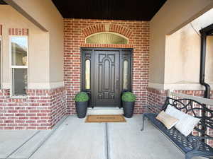 View of exterior entry with brick siding and a porch