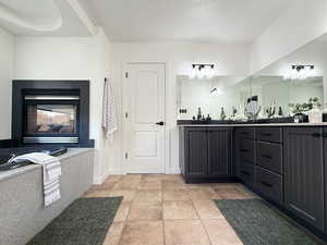 Bathroom with double vanity, light tile patterned flooring, a multi sided fireplace, and a textured ceiling