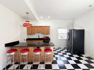 Kitchen featuring a peninsula, a breakfast bar area, dark flooring, freestanding refrigerator, and brown cabinets