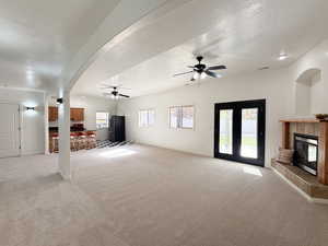 Unfurnished living room with arched walkways, light carpet, a textured ceiling, a tiled fireplace, and a ceiling fan