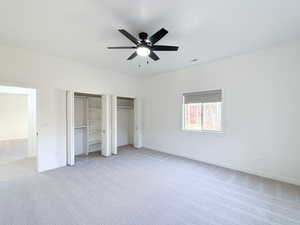 Unfurnished bedroom with multiple closets, light colored carpet, and ceiling fan