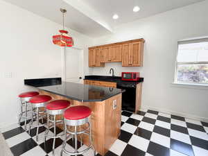 Kitchen featuring dark flooring, a peninsula, a breakfast bar, decorative light fixtures, and black dishwasher