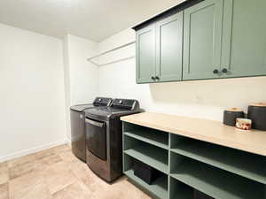 Laundry room featuring a textured ceiling, cabinet space, washer and clothes dryer, and light tile patterned floors