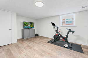 Exercise area with a textured ceiling and light wood-type flooring