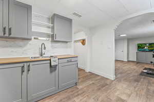 Kitchen featuring gray cabinetry, open shelves, arched walkways, tasteful backsplash, and butcher block counters