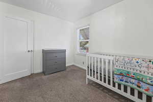 Bedroom featuring dark carpet and a nursery area