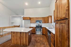 Kitchen with stainless steel appliances, brown cabinets, a kitchen island, dark wood-style floors, and tasteful backsplash