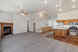 Kitchen with appliances with stainless steel finishes, high vaulted ceiling, open floor plan, dark carpet, and light countertops
