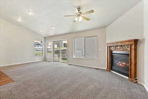 Unfurnished living room featuring a glass covered fireplace, a textured ceiling, lofted ceiling, carpet flooring, and a ceiling fan