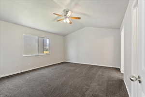 Spare room with dark carpet, vaulted ceiling, a textured ceiling, and ceiling fan