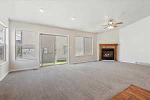 Unfurnished living room with vaulted ceiling, a glass covered fireplace, carpet flooring, and ceiling fan