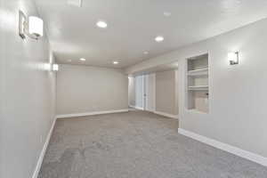 Empty room featuring light colored carpet, built in shelves, and recessed lighting