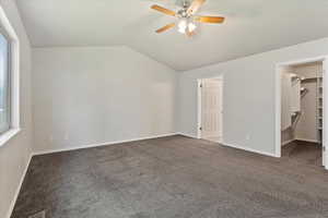 Unfurnished bedroom with carpet, a walk in closet, vaulted ceiling, and a ceiling fan