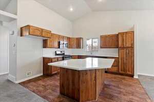 Kitchen featuring brown cabinets, a kitchen island, appliances with stainless steel finishes, high vaulted ceiling, and dark wood-type flooring