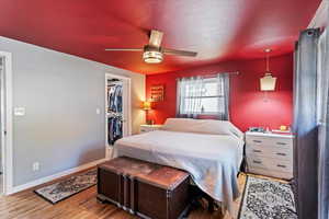 Bedroom with a walk in closet, laminate floors, a textured ceiling, and ceiling fan