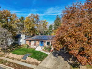 View of front facade featuring a front lawn, a chimney, and solar panels