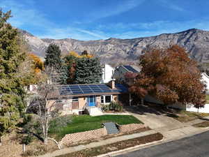 View of front of home featuring a mountain view, driveway, solar panels, a chimney, and a front lawn