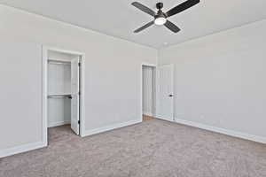 Unfurnished bedroom with a spacious closet, light carpet, and ceiling fan