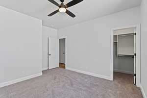 Unfurnished bedroom featuring a walk in closet, light colored carpet, and a ceiling fan