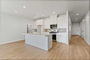 Kitchen with decorative backsplash, stainless steel appliances, a center island with sink, white cabinets, and recessed lighting