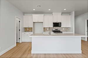 Kitchen featuring white cabinetry, stainless steel appliances, tasteful backsplash, light wood-style flooring, and recessed lighting