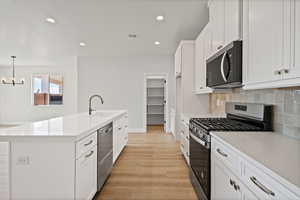 Kitchen featuring appliances with stainless steel finishes, white cabinetry, decorative backsplash, light wood-style flooring, and recessed lighting
