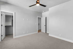Unfurnished bedroom featuring a walk in closet, light carpet, ceiling fan, and a textured ceiling