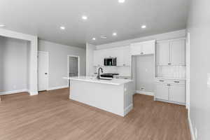Kitchen featuring white cabinets, tasteful backsplash, stainless steel microwave, a center island with sink, and recessed lighting