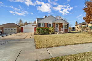 View of front of house with a front lawn, brick siding, a porch, concrete driveway, and a chimney