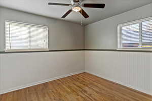 Empty room featuring wood finished floors, a ceiling fan, and a wainscoted wall