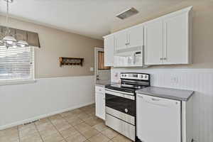 Kitchen with white appliances, white cabinetry, wainscoting, light tile patterned floors, and pendant lighting