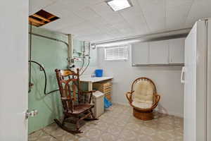 Below grade area with freestanding refrigerator, light flooring, and a drop ceiling