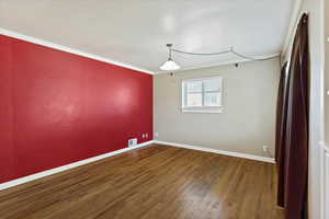 Empty room featuring crown molding and dark wood-type flooring
