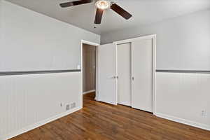 Unfurnished bedroom featuring dark wood finished floors, a closet, a ceiling fan, and a wainscoted wall