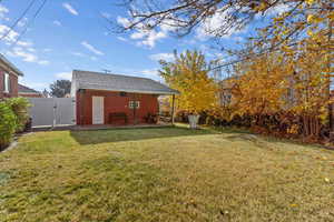 Back of house with a gate, a yard, a patio, roof with shingles, and brick siding