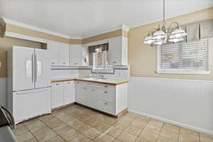 Kitchen with a wainscoted wall, white cabinets, freestanding refrigerator, tasteful backsplash, and tile countertops