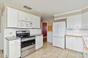 Kitchen with white appliances, white cabinetry, wainscoting, light tile patterned floors, and tile countertops