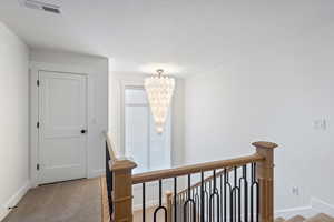 Hallway featuring an upstairs landing, loft, with upgraded carpet, and a textured ceiling