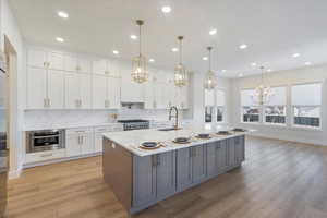 Kitchen featuring white cabinets, backsplash, light stone countertops, decorative light fixtures, and a spacious island